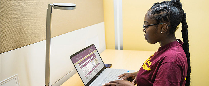 Student in maroon shirt at a laptop using Libraries Smart Search.