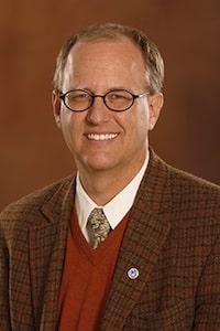 Professional headshot of Brad Swanson in a brown suit against a brown background.