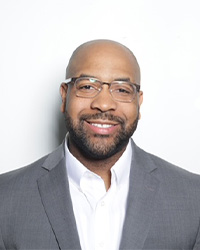 A man in a suit and glasses smiles for a professional headshot.