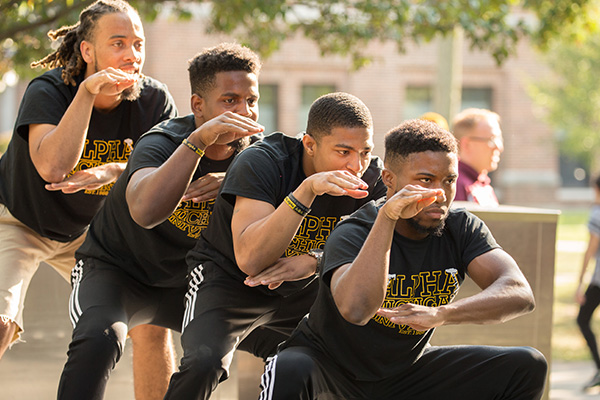 Four black male students wearing black t-shirts during a step performance