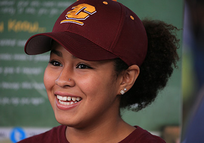 Close-up of a female student wearing a maroon baseball hat with a gold Action C logo on it.