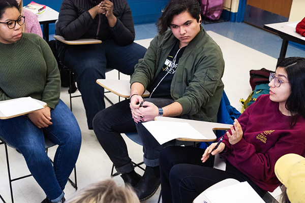 Several students sitting in a group in a classroom engaging in dialogue