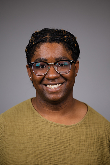 Professional headshot of a smiling Jasmine Asberry wearing a yellow shirt against a light grey background.