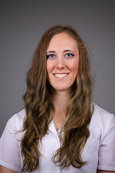 Professional headshot of a smiling Sarah Burgoyne wearing a white shirt against a grey background.