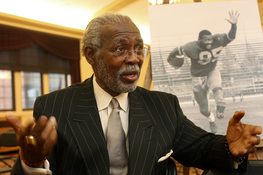 A man in a dark suit standing in front of a picture of a football player.