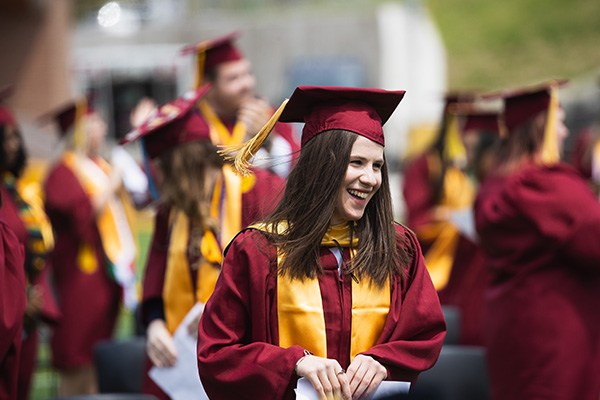 A student wearing a maroon cap and gown while smiling at graduation.