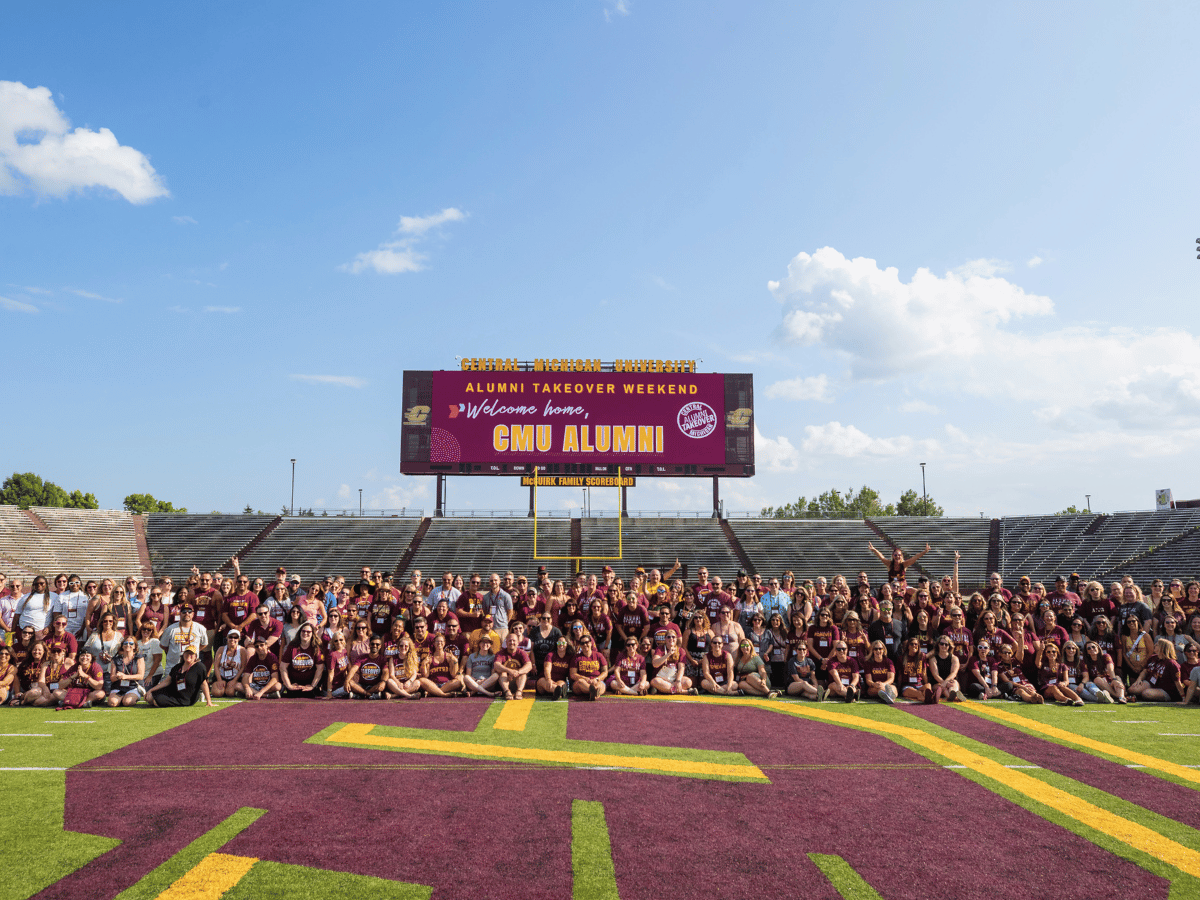 A large group of alumni on the football field in front of a welcome message.