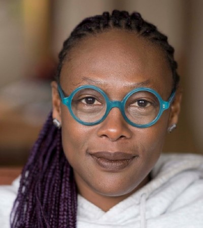 Nandi Comer, a woman with round, teal glasses and purple braids.