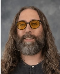 Professional headshot of Paul Zerkle in dark attire against grey background looking at camera