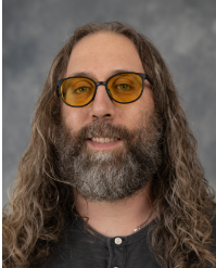 Professional headshot of Paul Zerkle in dark attire against grey background looking at camera