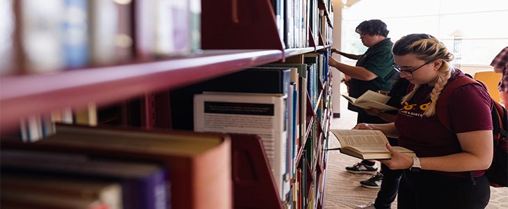 female student browsing books in the stacks at the Central Michigan University Libraries - Park Library