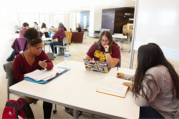 Three female students studying in 3 East at Central Michigan University Park Library with other students studying in the background.