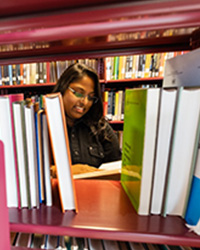 Still image of Sherly Tandra, a woman reading a book in a library surrounded by books.