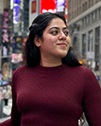 Still photo of graduating Libraries student employee Tejaswini Manohar in a maroon long sleeve shirt against a city billboard scape