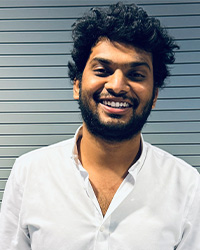 Still photo of graduating student Si Teja Puli in a white collared button shirt against a striped background