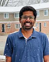 Still photo of Sai Chand Venapally in a blue polo with brick/wood building in the background