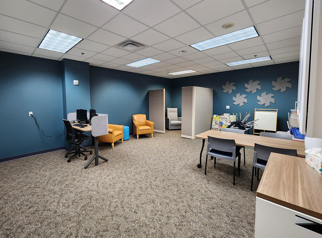 Family Friendly Study Room at CMU Libraries with two blue walls computer station, mustard yellow chairs, table, play area with easel, lactation room.