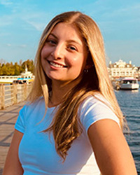 Headshot of Racheal Ruttenberg in a white shirt with beach scape background