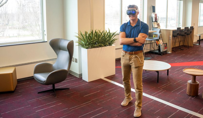 A man with a blue shirt is standing in the Adobe Lounge in the Park Library wearing virtual reality goggles.