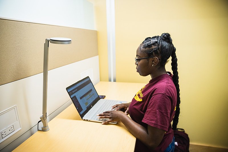 student at laptop student wearing maroon and gold t shirt and working at laptop in the library