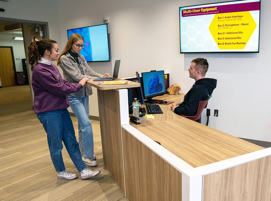 Two students looking at a laptop and asking questions to an Adobe Support student seated behind the desk in tthe Adobe Digital Lounge