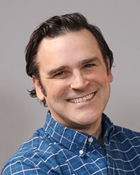 Andy Blom wearing a blue shirt while posing for a professional headshot.