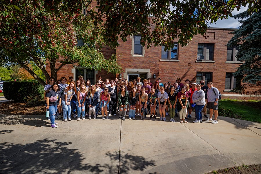 A group of Central Michigan University Honors Program students stand together in front of Powers Hall.
