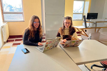 Two women sitting at a table with laptops.