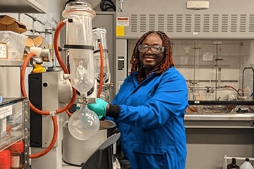 A student wearing a blue lab coat working in the laboratory.