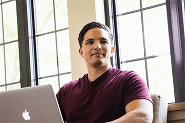 A man with a laptop sitting in front of a window.