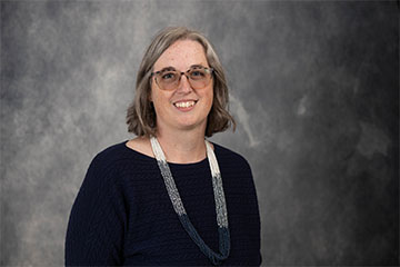 A smiling woman wearing glasses and a blue sweater.