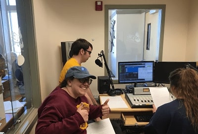 Three people working in an audio room with a microphone and computers.