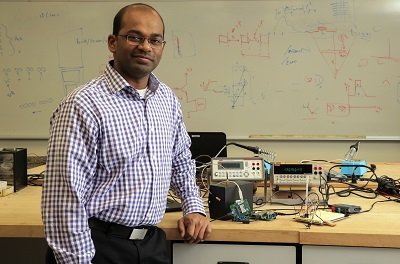 Dr. Kumar Yelamarthi leaning against a table while wearing a blue and white button up shirt.