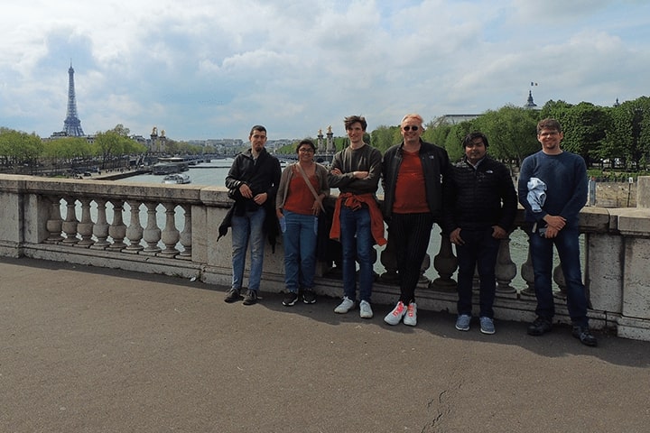 A group of six people posing for a picture in front of the Eiffel Tower.