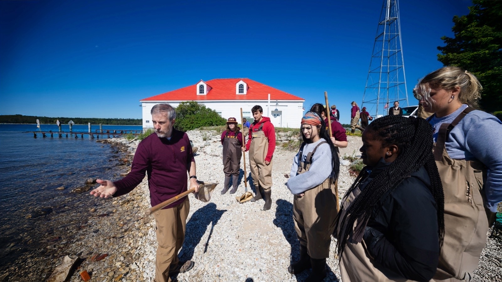 A group of students in waders stand on a rocky beach with a CMU faculty member.