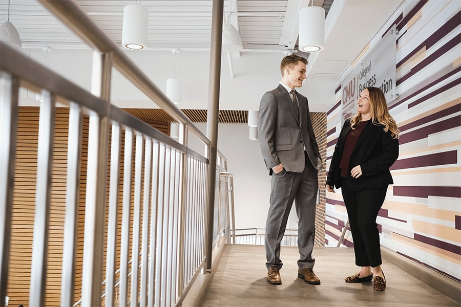 A man and woman standing near a staircase in front of a CMU College of Business Administration sign.