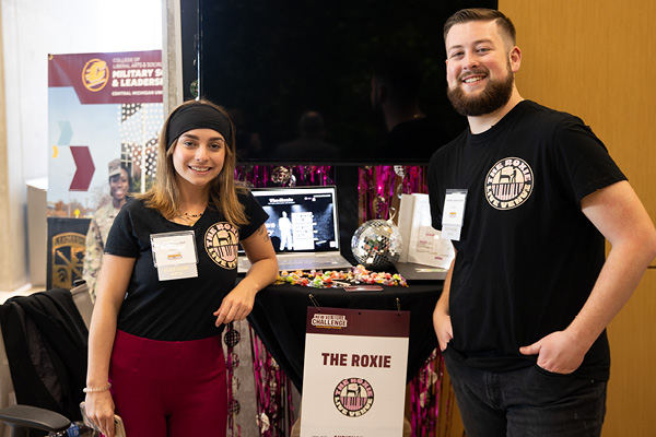 Two students standing in front of their venture gallery table at the 2024 New Venture Challenge.