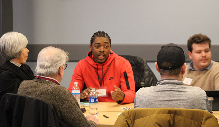 A student speaking with three faculty members at a table in a classroom.