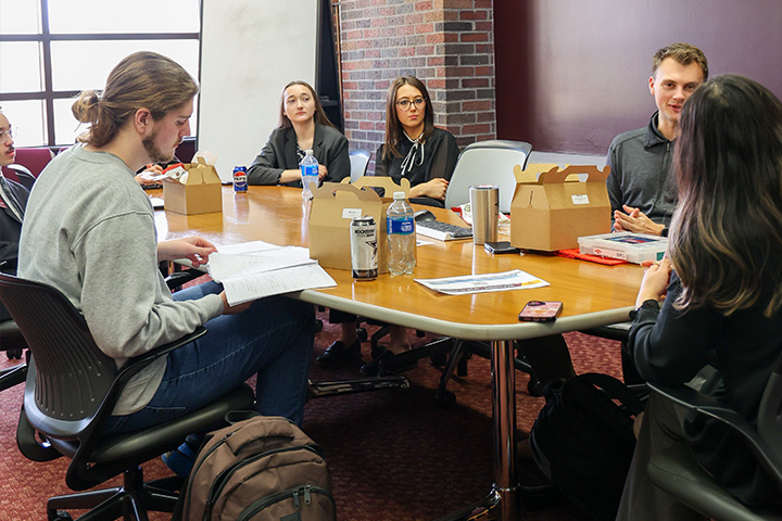 Students eat lunch with representatives from Dow during a career event. The breakout session took place in the Rico conference room. The participants have open lunch boxes in front of them.