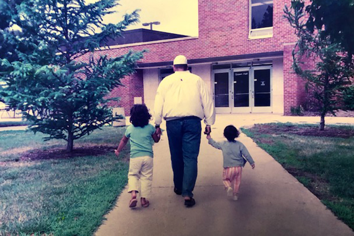 Lee Curtis walks hand in hand with two young children along a sidewalk toward Grawn Hall at Central Michigan University.