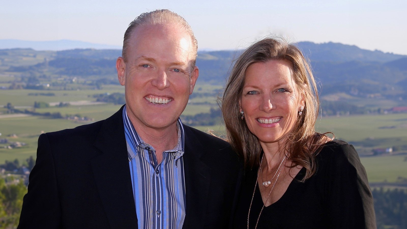 James and Renaye Damman are standing in front of an idyllic, valley town in summer.