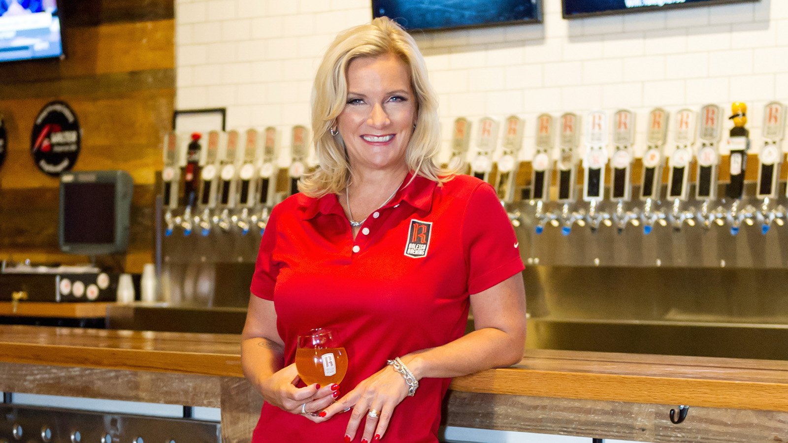 Kristie Nystedt standing in front of a bar, holding a wine glass full of her beer.