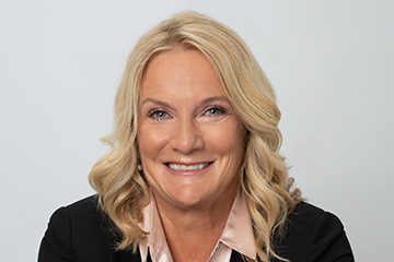 Kristie Nystedt wearing a peach colored blouse and dark jacket in a professional headshot.