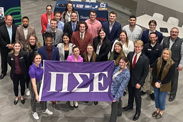 Members of Pi Sigma Epsilon hold a PSE flag on the Grawn Atrium staircase.