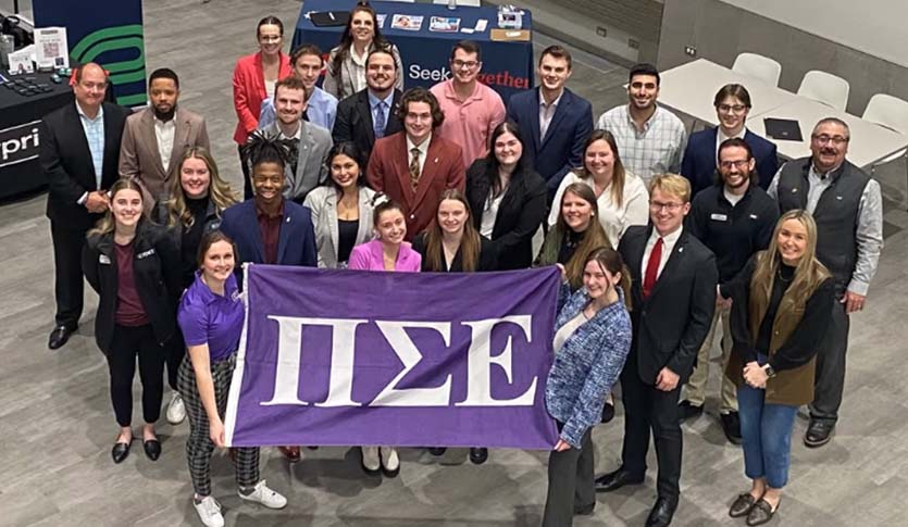 Members of Pi Sigma Epsilon hold a PSE flag in the Grawn Atrium.