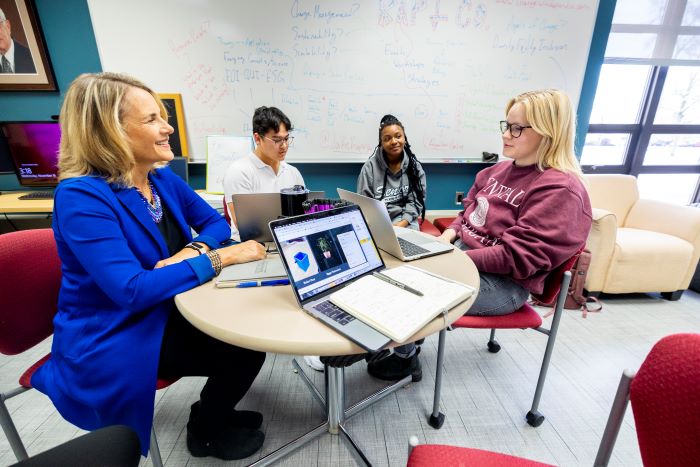 A faculty member mentoring three students sitting around a table in the IDEA Den.