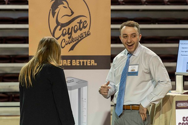 A student smiling and standing next to his venture display table at the 2023 New Venture Challenge.