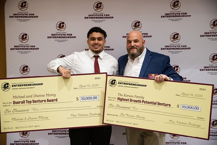 A student standing with a cmu faculty member holding up the student's two winning checks during the 2024 New Venture Challenge