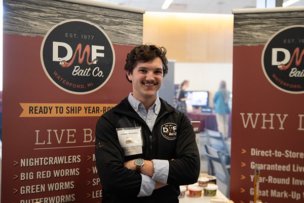 A student smiling and standing in front of his venture display at the 2024 New Venture Challenge.