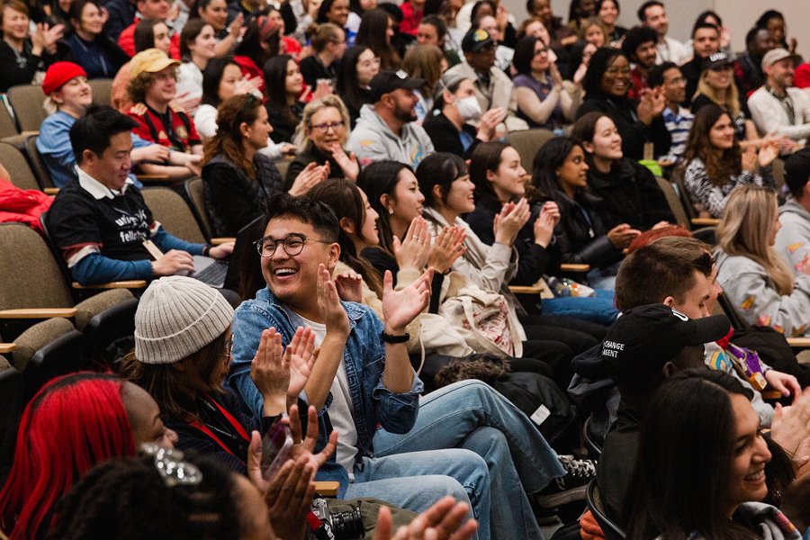 A crowd of students sitting in an auditorium clapping.